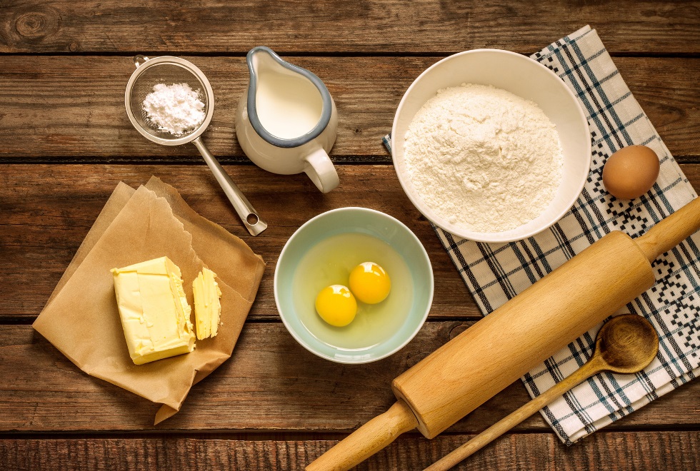 Tisch mit Backzutaten wie Mehl, Butter, Eiern und Geräten wie Teigrolle und Sieb
