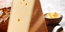 großes Käsestück vor einem Laib Brot und einem Schälchen mit Butter