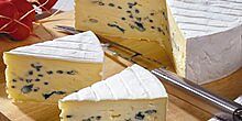 Laib mit zwei herausgeschnittenen Ecken Blauschimmelkäse auf Käsebrett mit Käsemesser