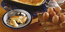 Mehlkuchen auf Teller mit Löffel, daneben Auflaufform mit Mehlkuchen, daneben mehrer braune Eier