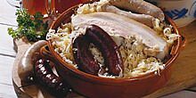 Kesselfleisch, sowie Leber- und Blutwürste in einem Topf mit Sauerkraut, zwei weitere Würste auf einem Holzbrett