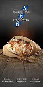 Brot in Leinensack am Boden liegend mit schwarzem Hintergrund; dahinter Schriftzug „Kulinarisches Erbe Bayern“